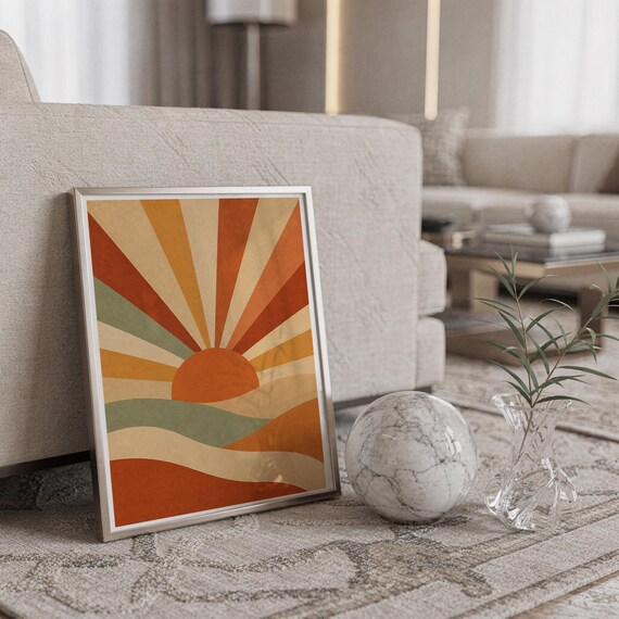 Retro geometric sunrise print in a silver frame leaning against a sofa beside a decorative marble sphere.