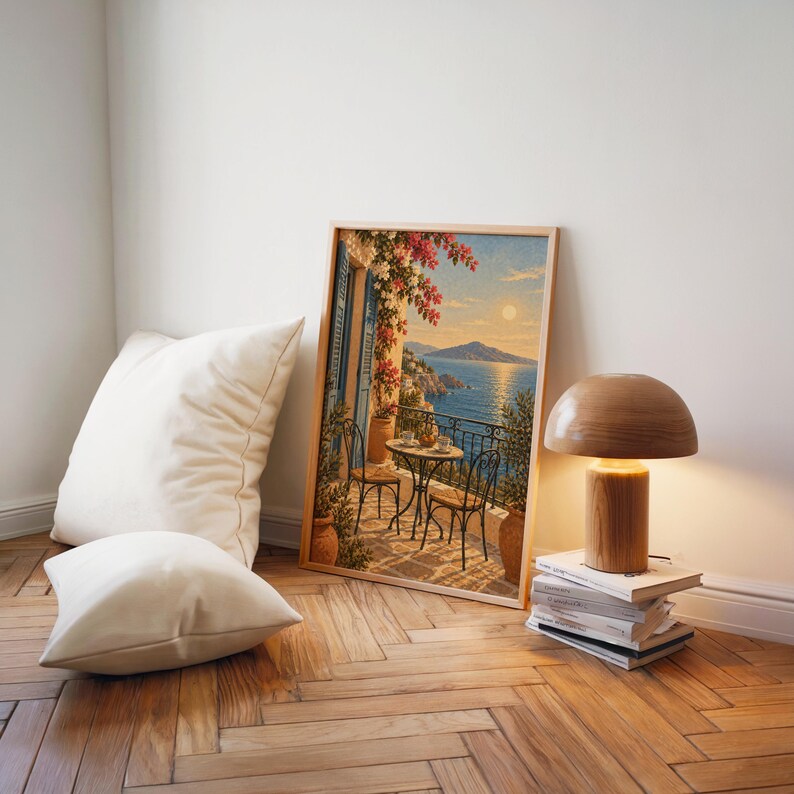 Mediterranean balcony wall art print leaning on a herringbone wood floor beside cream cushions and a wooden mushroom lamp.