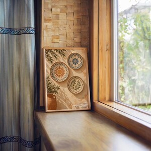 Mediterranean ceramic plate wall art print standing on a wooden window sill in warm natural light.