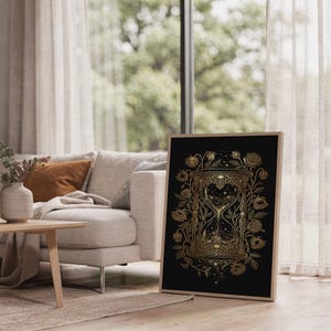 Gothic hourglass wall art print leaning on the floor beside a cream armchair next to large garden windows.