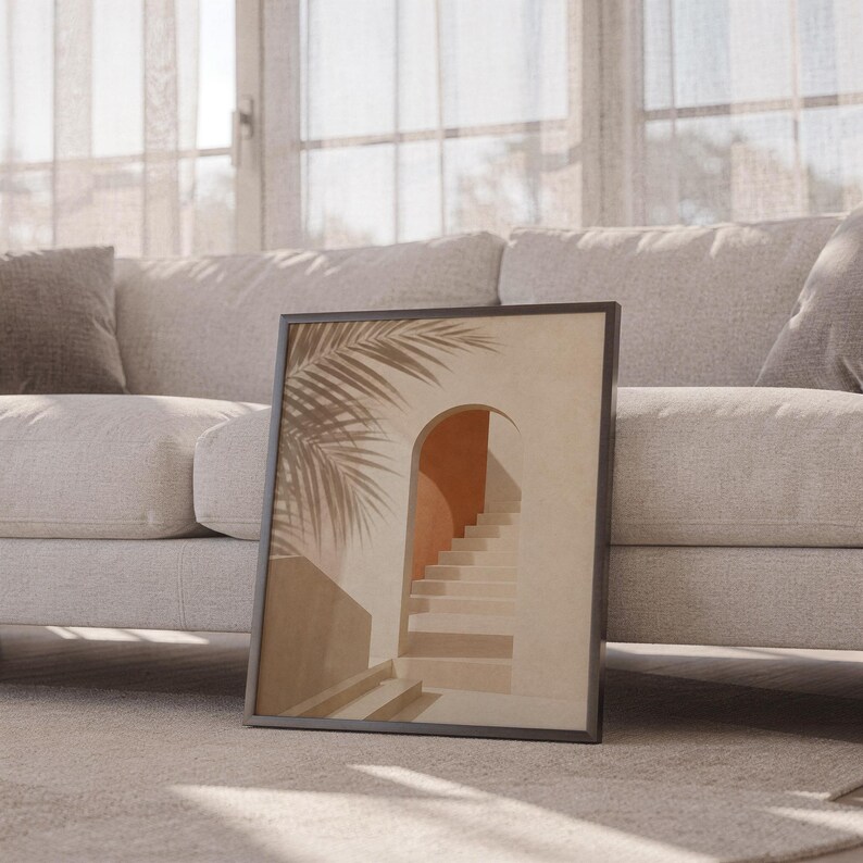 Black framed palm leaf wall art resting on the floor beside a white sofa.