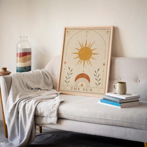 Japandi celestial sun print in wooden frame resting on beige sofa with cozy blanket and books