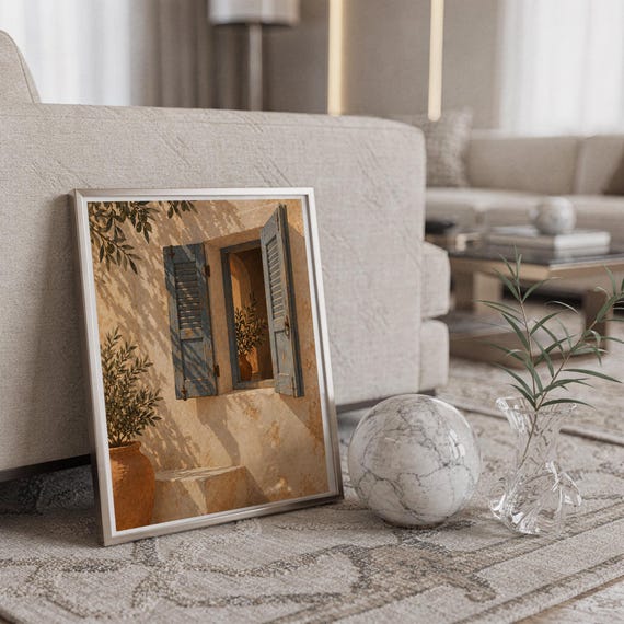 Mediterranean blue shutter wall art print in a silver frame leaning against a sofa beside a decorative marble sphere.