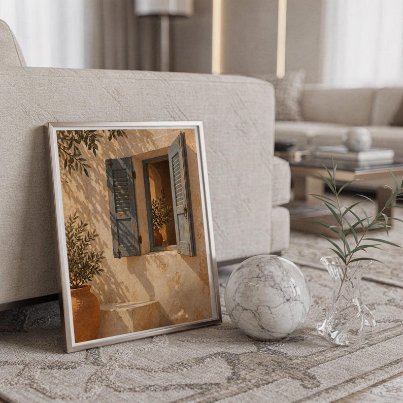 Mediterranean blue shutter wall art print in a silver frame leaning against a sofa beside a decorative marble sphere.