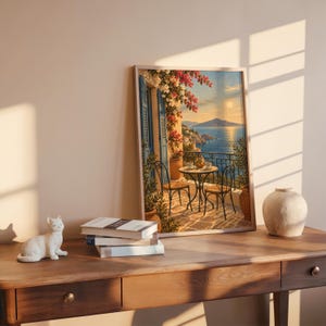 Mediterranean balcony wall art print leaning on a wooden desk against a warm beige wall in soft window sunlight.
