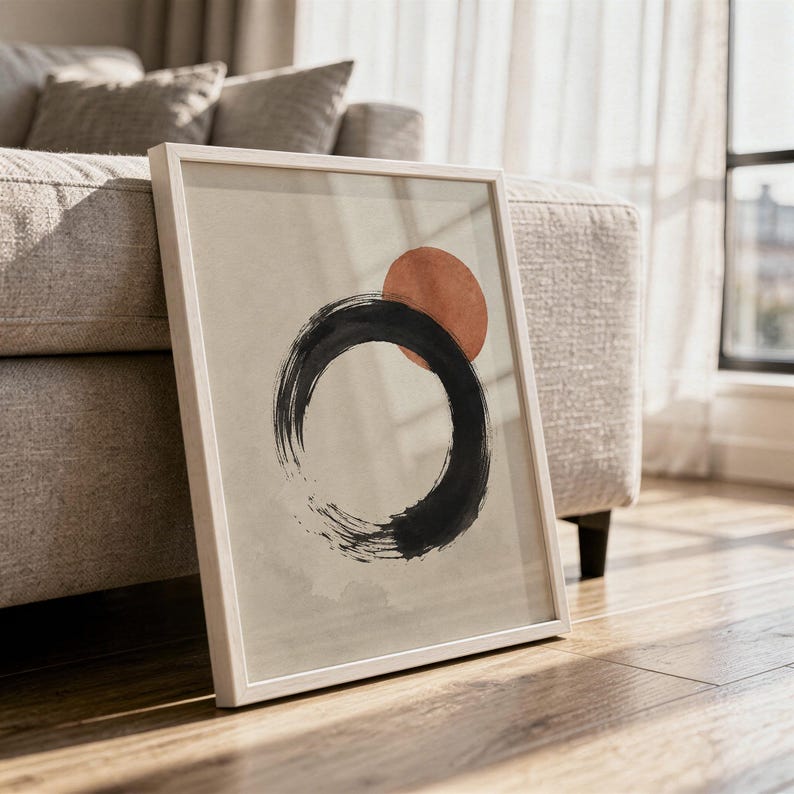 Close-up view of a framed abstract black circle print leaning on a light-colored wooden floor.