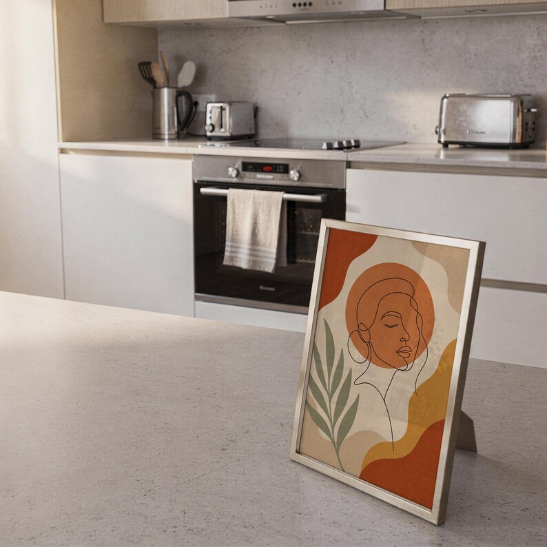 Abstract line art face print standing on a countertop in a modern white kitchen.