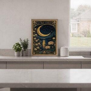 A framed Art Nouveau moon poster stands on a kitchen counter next to two small potted plants.