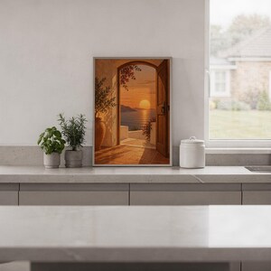 Mediterranean sunset doorway wall art print standing on a white kitchen counter beside potted herbs.