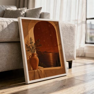Mediterranean night sea wall art print in a white frame leaning against a gray sofa on a sunlit wooden floor.
