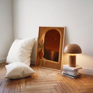 Mediterranean night sea wall art print leaning on a herringbone wood floor beside cream cushions and a wooden mushroom lamp.