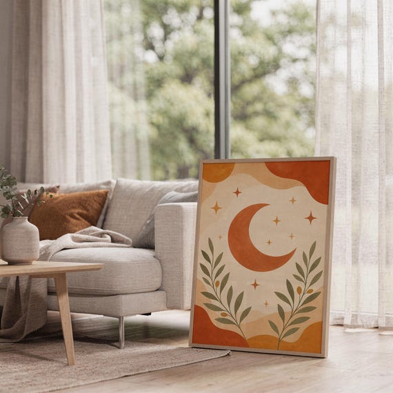 Terracotta crescent moon and olive branch print leaning on the floor beside a cream armchair next to large garden windows.
