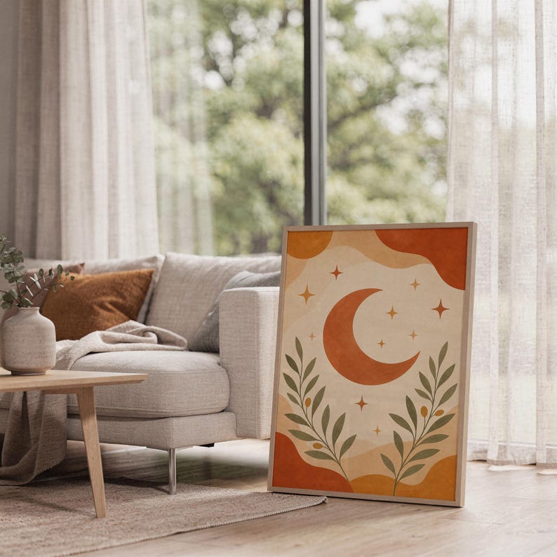 Terracotta crescent moon and olive branch print leaning on the floor beside a cream armchair next to large garden windows.