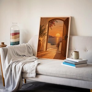 Mediterranean sunset doorway wall art print leaning on a cream sofa against a beige wall beside books and a mug.