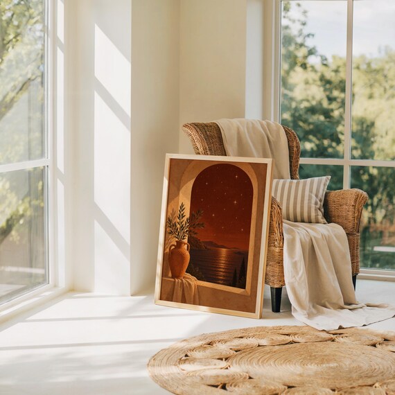 Mediterranean night sea wall art print leaning on the floor beside a rattan armchair and jute rug in a bright sunlit room.