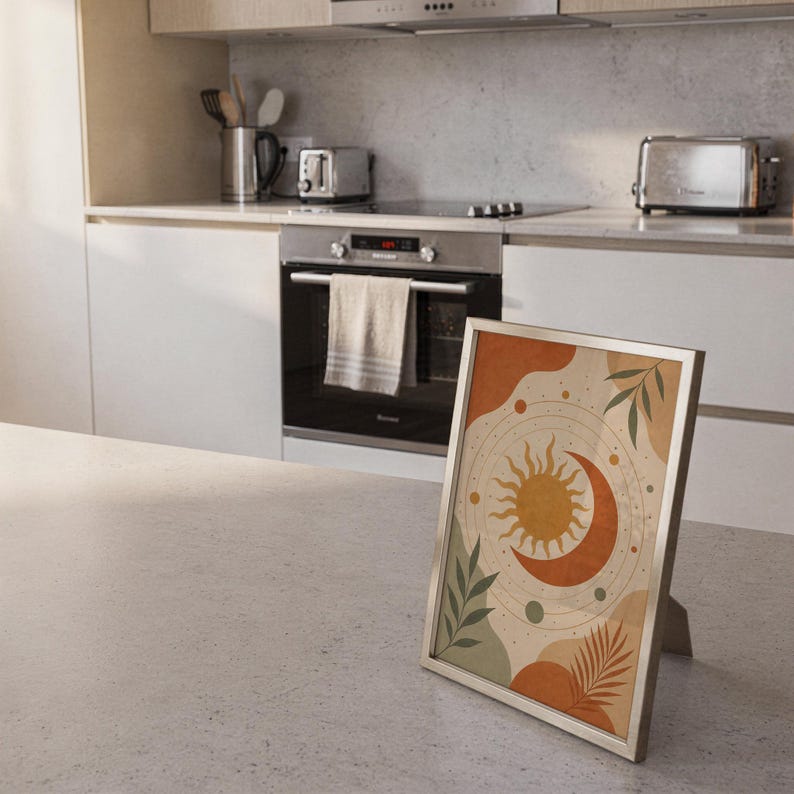 Celestial sun and moon art print standing on a countertop in a modern white kitchen.