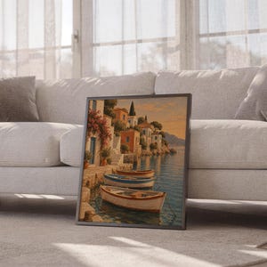 Mediterranean coastal village wall art print leaning against a white sofa in a bright living room with sheer curtains.