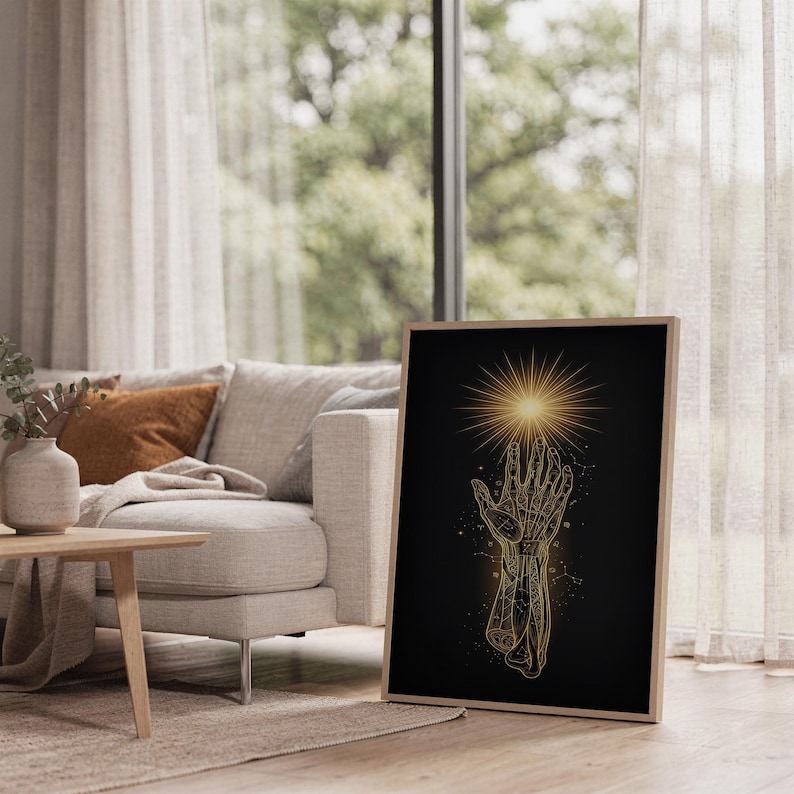 Celestial hand wall art print leaning on the floor beside a cream armchair next to large garden windows.