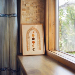 Warm aesthetic framed celestial art print resting on a wooden windowsill overlooking nature⁠
