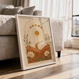 Celestial sun and moon wall art print in a white frame leaning against a gray sofa on a sunlit wooden floor.
