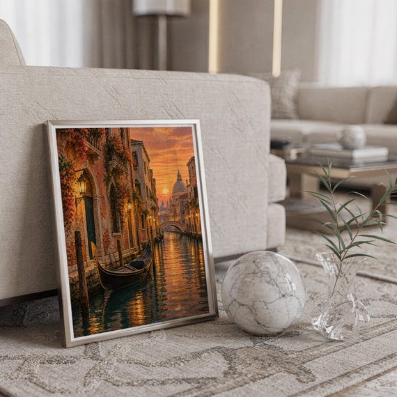 Venice canal sunset wall art print in a silver frame leaning against a sofa beside a decorative marble sphere.