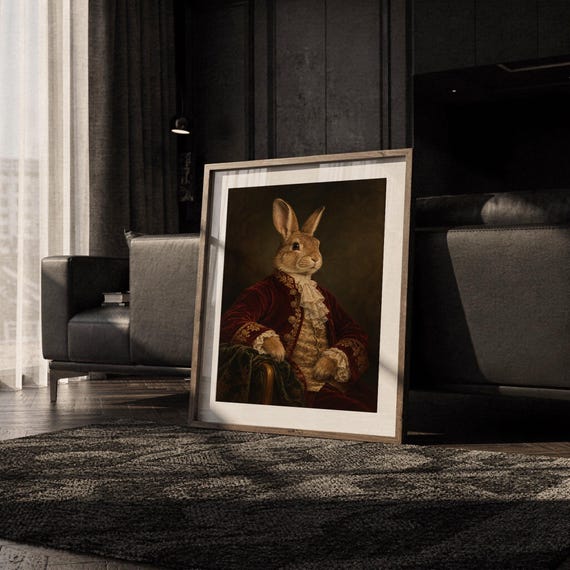 Regal rabbit portrait wall art print leaning on the floor beside a cream armchair next to large garden windows.