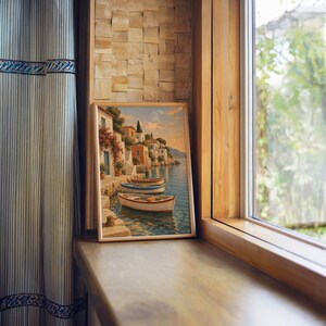 Mediterranean coastal village wall art print standing on a wooden window sill in warm natural light.