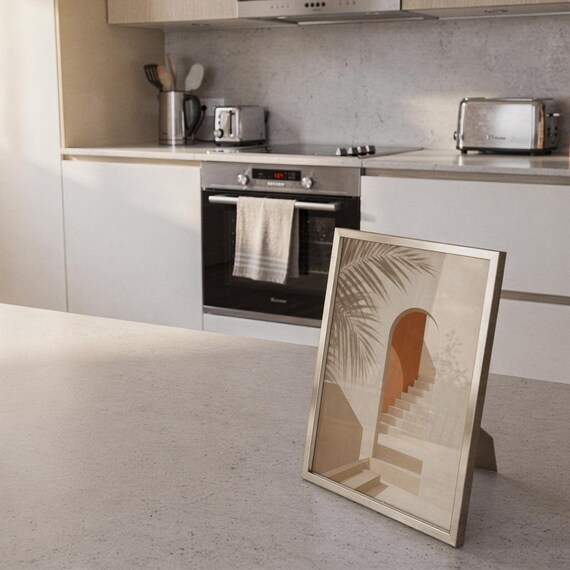 Small framed abstract art piece leaning against the backsplash on a modern white kitchen counter.