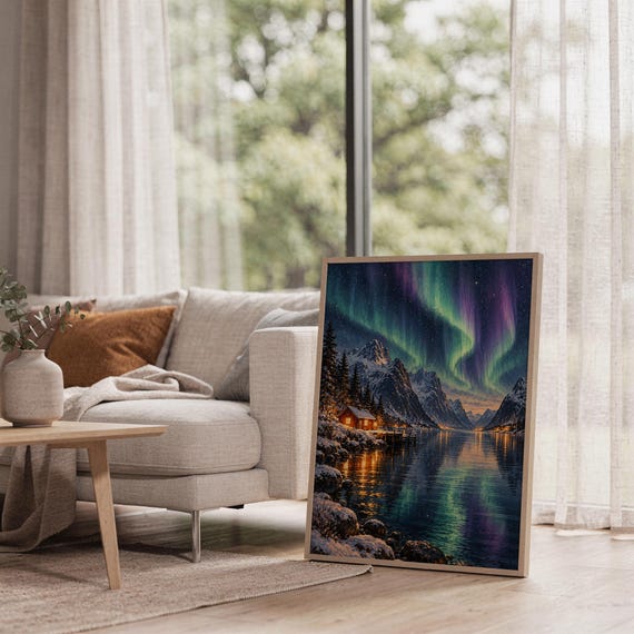 Aurora borealis mountain landscape wall art print leaning on the floor beside a cream armchair next to large garden windows.