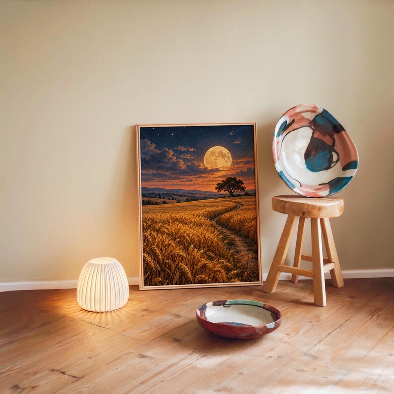 Moon wall art print leaning against a warm beige wall on a wooden floor beside a stool and a glowing lamp.
