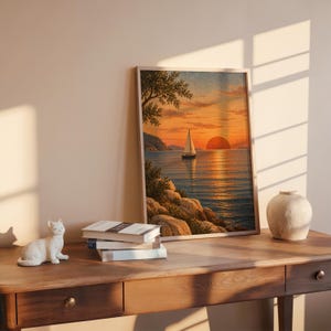 Sunset sailboat wall art print leaning on a wooden desk against a warm beige wall in soft window sunlight.