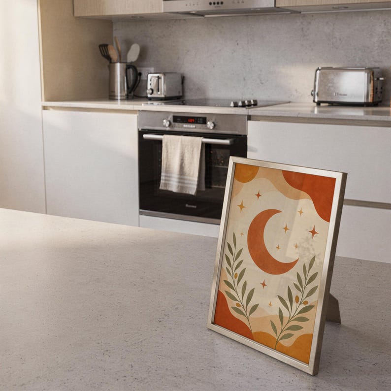 Terracotta crescent moon and olive branch print standing on a countertop in a modern white kitchen.