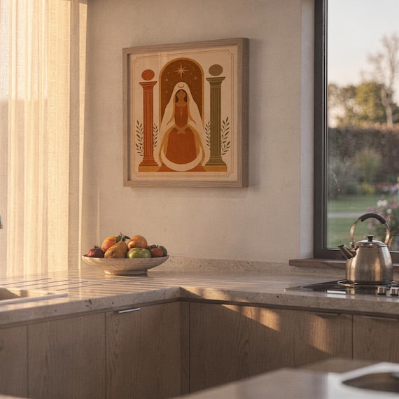 Framed terracotta architectural poster hanging on a sunny kitchen wall beside a countertop with fresh fruits.