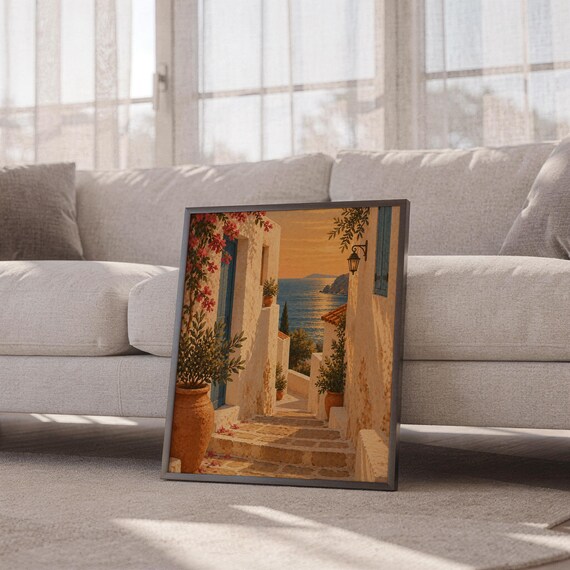 Mediterranean coastal village wall art print leaning against a white sofa in a bright living room with sheer curtains.