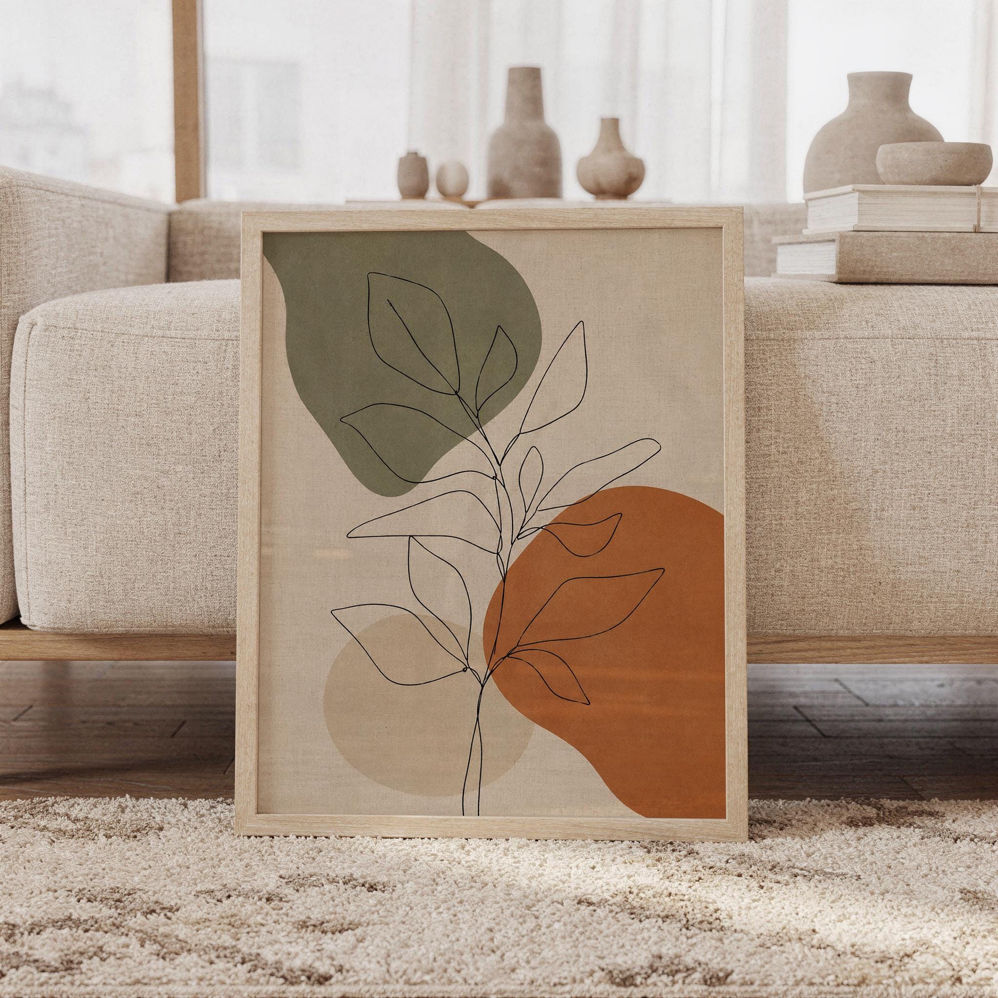 Framed mid century botanical leaf poster resting on rug next to beige sofa