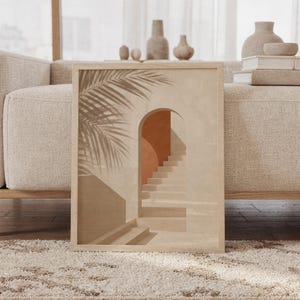 Framed terracotta arch and boho stairs print resting on rug next to neutral couch