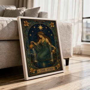 The star tarot card wall art print in a white frame leaning against a gray sofa on a sunlit wooden floor.