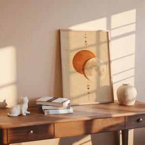 Sun and moon celestial wall art print leaning on a wooden desk against a warm beige wall in soft window sunlight.