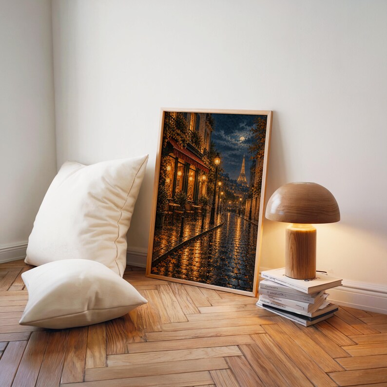 Paris eiffel tower wall art print leaning on a herringbone wood floor beside cream cushions and a wooden mushroom lamp.