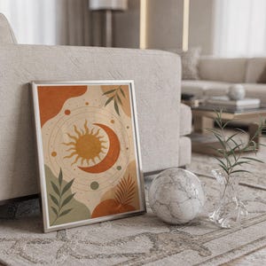 Celestial sun and moon art print in a silver frame leaning against a sofa beside a decorative marble sphere.