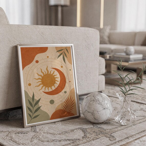Celestial sun and moon art print in a silver frame leaning against a sofa beside a decorative marble sphere.