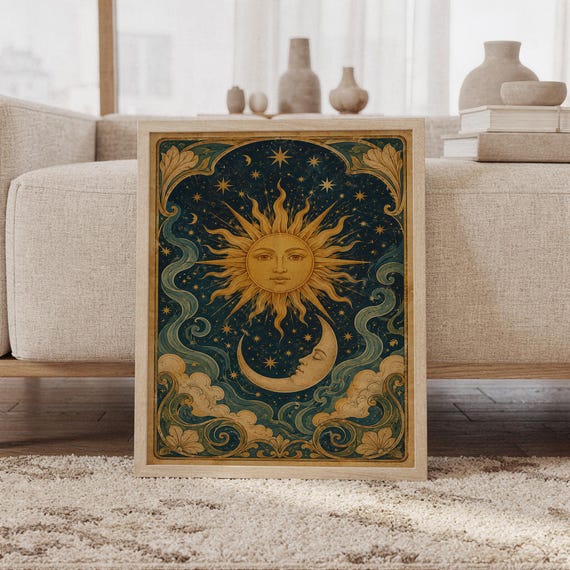 Celestial sun and moon wall art print featuring antique gold sun rays, a crescent moon, twinkling stars, deep navy blue skies, teal swirling clouds, and ornate botanical borders in a vintage celestial style, framed and leaning against a beige sofa on a textured rug in a bright Scandinavian living room.