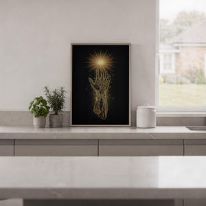 Celestial hand wall art print standing on a white kitchen counter beside potted herbs.