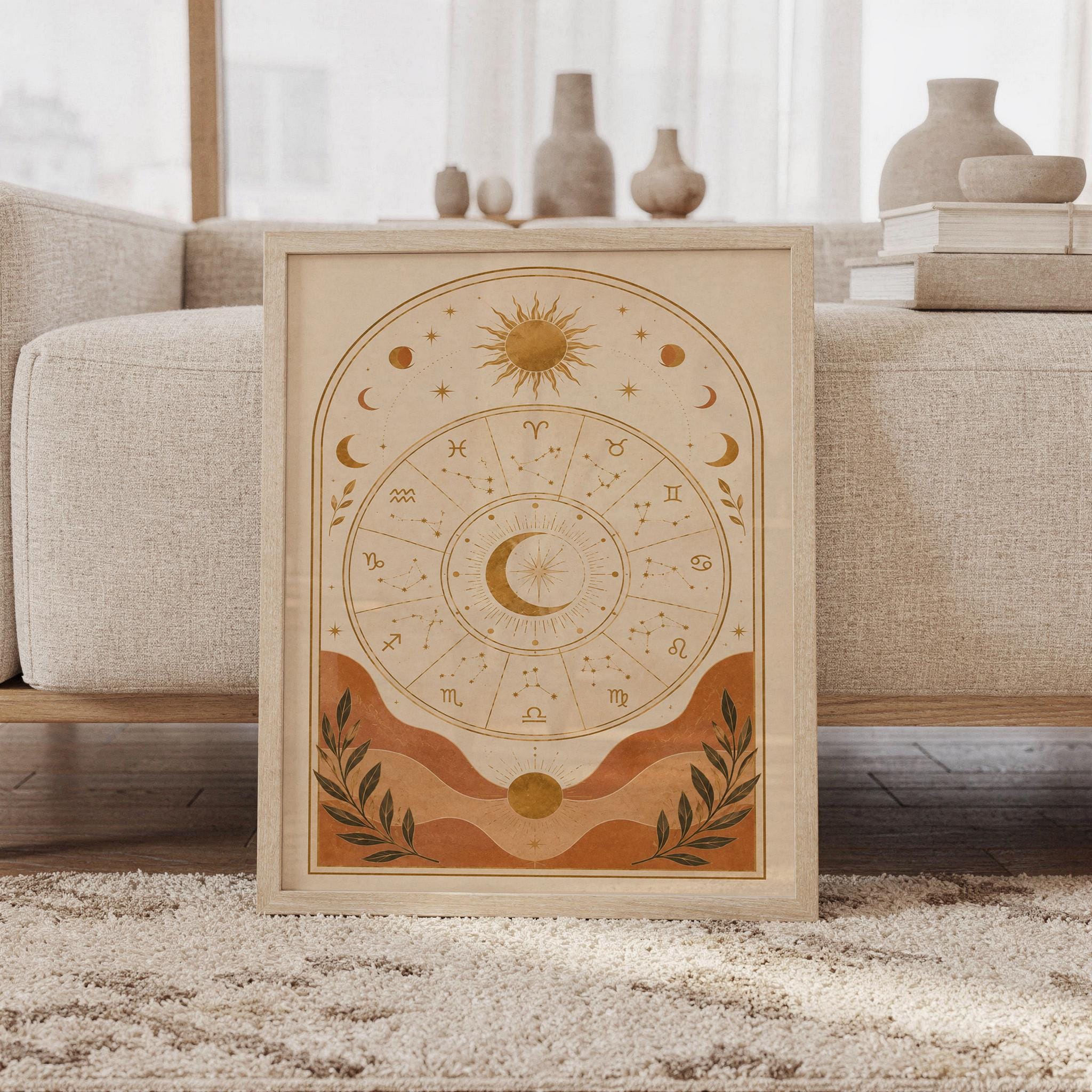 Zodiac wheel wall art print featuring warm ochre gold, terracotta, cream, and deep olive accents, celestial sun and moon motifs, zodiac symbols, and delicate constellation details in a vintage boho style, framed and leaning against a beige sofa on a textured rug in a bright Scandinavian living room.