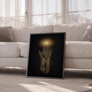 Celestial hand wall art print leaning against a white sofa in a bright living room with sheer curtains.