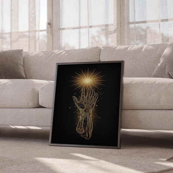 Celestial hand wall art print leaning against a white sofa in a bright living room with sheer curtains.