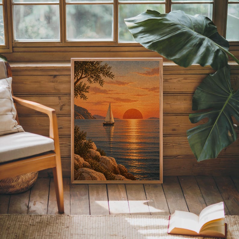 Sunset sailboat wall art print leaning against warm wood paneling beside a wooden armchair and a monstera plant.