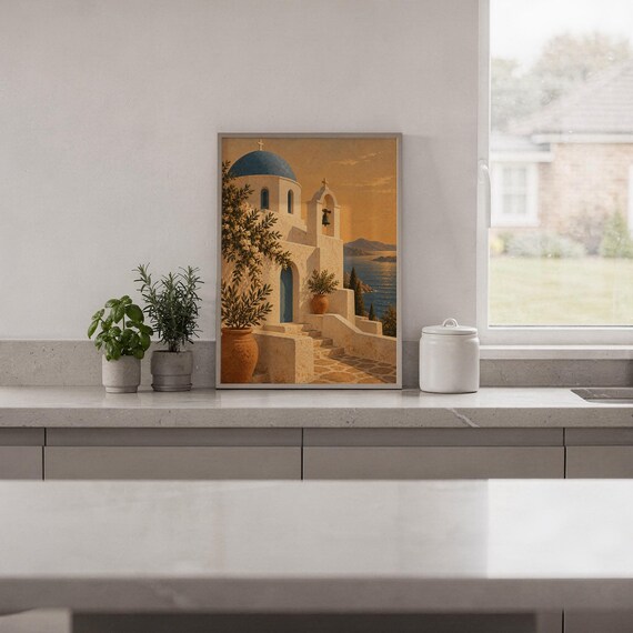 Santorini church wall art print standing on a white kitchen counter beside potted herbs.