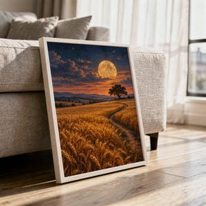 Moon wall art print in a white frame leaning against a gray sofa on a sunlit wooden floor.