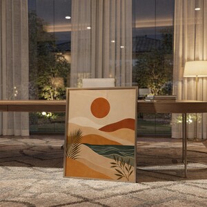Modern abstract landscape poster framed and leaning on wooden floor next to floor lamp in living room.